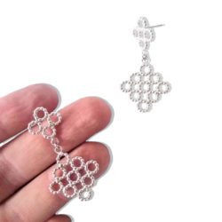 Silver Beaded Quatrefoil Dangle Earrings - one earring held on palm of hand, other earring on white background nearby