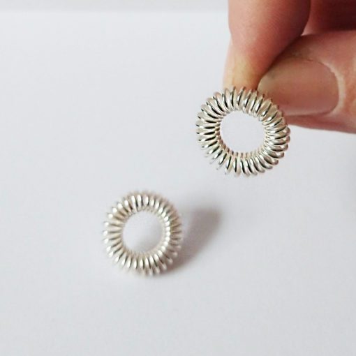 Silver round coil stud earrings - one held between index finger and thumb, other lying on white background