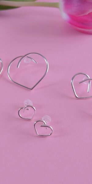 Silver Heart Stud Earrings collection by Essemgé - 3 pairs of silver earrings in 3 different sizes, on pink background